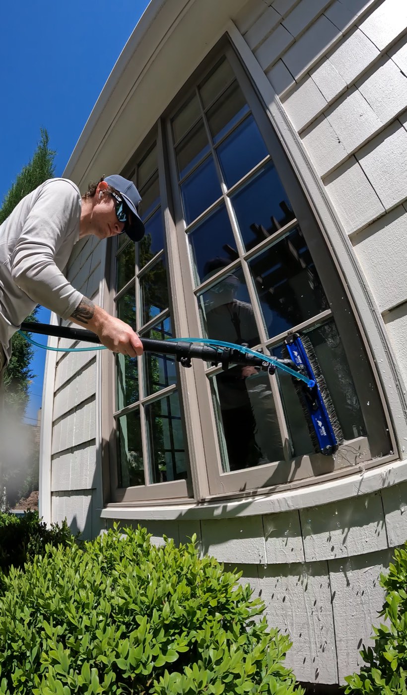 Alternative Window Cleaning technician cleaning a bay window with a water-fed pole in Johnson County, KS